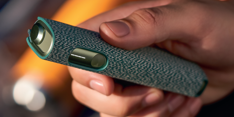 Hands holding smartphones and one IQOS device.