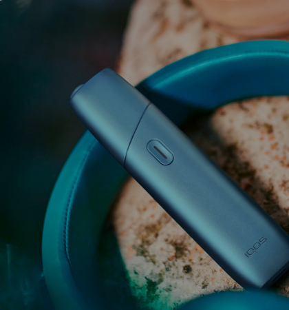 IQOS Originals One device next to turquoise headphones.