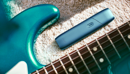 IQOS Originals One device next to turquoise headphones.