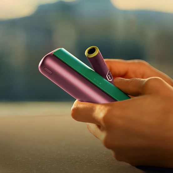 Hand holding IQOS Originals Duo holder and pocket charger in turquoise color.