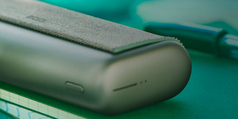 A woman holding an IQOS device looking at a laptop.