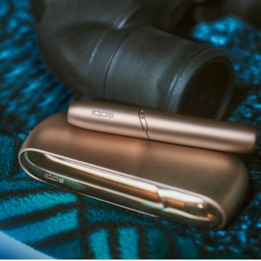 Brilliant gold IQOS 3 DUO with HEETS stick in hand and charger