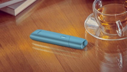 Turquoise IQOS Originals One device on a desk next to a tea cup.